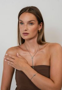Silver jewelry featuring a thin snake chain with a bead accent on a model wearing a brown strapless top. Smooth texture, minimalist design.