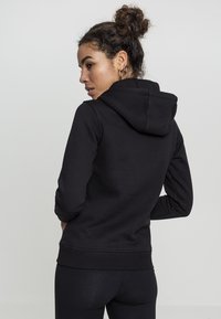 Sudadera negra con capucha, ajustada con puños y dobladillo acanalados, textura suave, diseño simple, vista desde la parte de atrás.