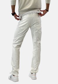 Jean en denim blanc à coupe ajustée, avec deux poches arrière, texture subtile, et associé à des baskets blanches. Design simple et moderne.