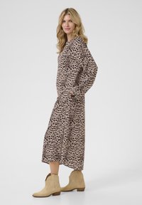 Rochie maxi cu imprimeu leopard dintr-un material moale, cu mâneci lungi, buzunare laterale și un tiv ușor evazat, asortată cu cizme de glezna bej.