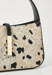 Beige and black spotted fabric handbag with a black leather strap and gold hardware accent. Rounded shape, textured surface, compact design.