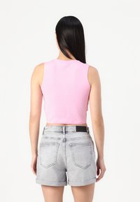 Roosa lühikeste varrukatega tank top, mis on valmistatud pehmest kangast, koos heledate hallide denim-lühikeste pükstega, millel on volditudääred ja tagataskud.