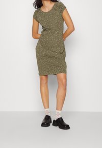 Zielono-oliwkowa sukienka w kwiaty z krótkimi rękawami, okrągłym dekoltem i dopasowanym krojem. Połączona z czarnymi klapkami i wzorzystymi pastelowymi skarpetkami.