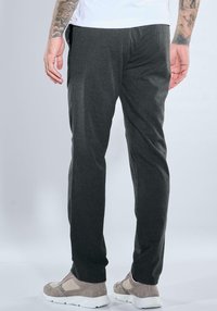 Dark grey trousers made of a textured fabric, featuring a tapered fit. Worn with light grey sneakers, showing clean lines and minimal details.