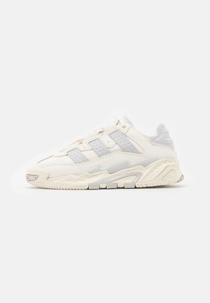 Lavtskåret chunky sneaker i off-white med teksturerede paneler, tyk sål og snørebånd vist mod en ensfarvet baggrund.