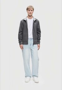 Grå t-skjorte med glidelås og lysegrå krage, brukt over en hvit t-skjorte, sammen med lyseblå jeans og hvite joggesko.