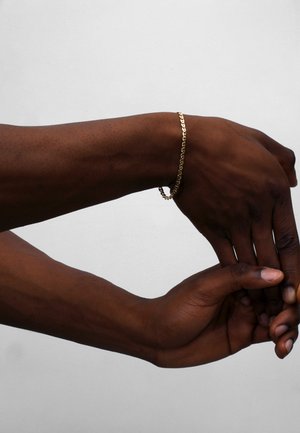 Goldene Kettenarmband an einem Handgelenk, mit einem verknüpften Design. Der Hautton steht im Kontrast zu dem glänzenden metallischen Finish und hebt den Schmuck hervor.
