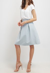 Gonna svasata azzurro chiaro con motivo a rilievo, abbinata a una maglietta bianca a maniche corte. L'outfit è completato da tacchi beige con cinturini.