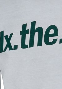 Hellgraues Baumwoll-T-Shirt mit fettgedrucktem, dunkelgrünem Text "fix.the." auf der Vorderseite, mit weicher Textur und lässigem Schnitt.