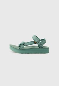 Teva sandals with a platform sole in a teal color. Features adjustable straps made of fabric and textured surface for grip.