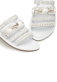 White sandals with three beaded straps featuring seashell and pearl accents. Smooth leather footbed and light-colored textured outsole.