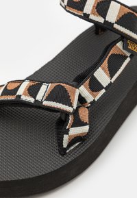 Chanclas negras con suela texturizada, con cómodas tiras anchas en colores negro, crema y óxido. Ligeras y duraderas.