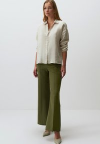 Lichtbeige linnen shirt met knoopsluiting en opgerolde mouwen, gedragen met hooggetailleerde olijfgroene wijde broek en gestructureerde neutrale hakken.