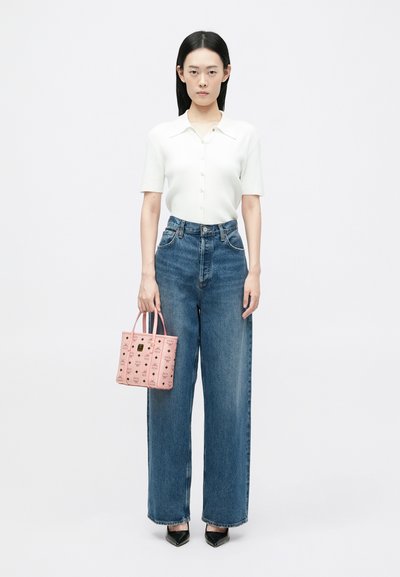 Biała prążkowana bluzka z krótkim rękawem i detalem guzika, niebieskie dżinsy z wysokim stanem i szerokimi nogawkami, różowa torba w wzory oraz czarne szpilki.