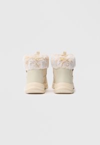 Botas de tornozelo bege apresentam um suave acabamento de pele de pelúcia branca na gola, um material superior liso e uma sola texturada para melhor aderência.