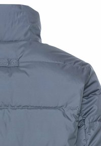 Grijze pufferjack met een hoge kraag, voorzien van horizontale gestikte naden en een klein logolabel bij de hals. Gladde synthetische stof.