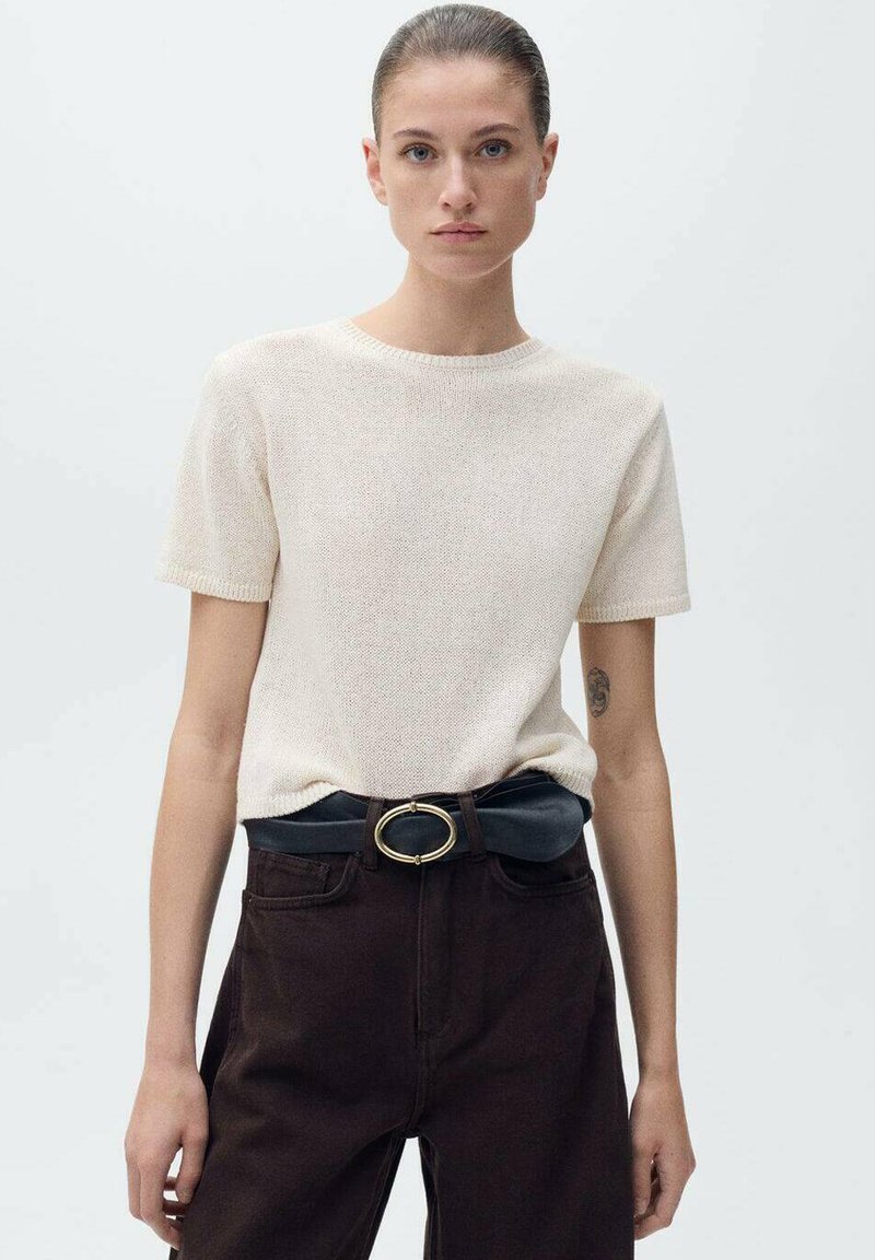 Ljus beige kortärmad stickad topp tillsammans med mörkbruna hög midjebyxor. Har ett svart bälte med en gyllene oval spänne.