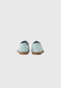 Zapatillas ligeras de color azul claro sin cordones, con parte superior de ante perforado, puntera redondeada y suela de goma marrón. Tacón ligeramente elevado.