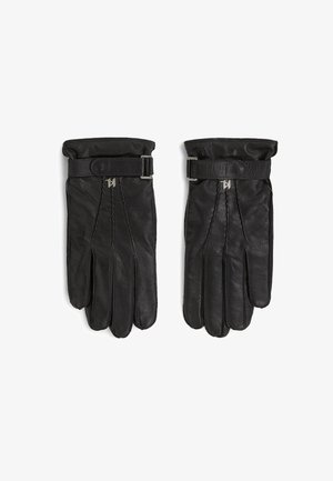 Par sorte læderhandsker med håndledsremme og metal spænde detaljer, lagt fladt side om side på hvid baggrund.