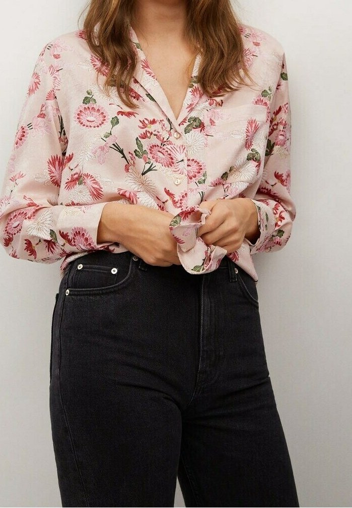 Blouse à manches longues, rose à motif floral avec boutons sur le devant ; tissu semblant léger avec une texture douce ; portée avec un jean noir taille haute.