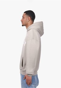 Hoodie in Hellgrau mit Kängurutasche, gerippten Bündchen und Saum sowie Logodruck auf der Vorderseite. Glatte Textur.
