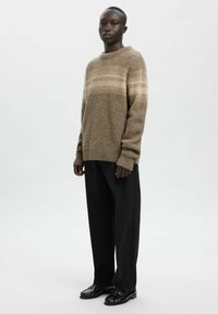 Pull en maille marron avec fines rayures horizontales claires, encolure ronde, poignets côtelés, associé à un pantalon large noir et des chaussures noires.