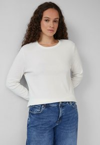 Weißes, geripptes Langarmshirt mit rundem Ausschnitt, kombiniert mit blauen Jeans im klassischen Fünf-Taschen-Design.