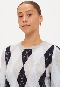 Γκρι πουλόβερ με σχέδιο argyle σε ανοιχτό μπλε, σκούρο μπλε και κρέμα. Στρογγυλή λαιμόκοψη και ραμμένες μανσέτες. Λείος υφασμάτινος χαρακτήρας, μέτρια πάχος.