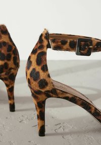 Leopardenmuster High Heels mit einer suedartigen Textur, einem dünnen Knöchelriemen mit einer quadratischen schwarzen Schnalle und einem Stiletto-Design.