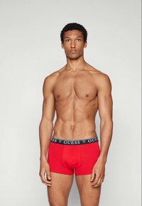 Røde boxershorts laget av bomull, med et svart elastisk midjebånd med "GUESS"-logo. Jevn tekstur og tettsittende design for komfort.