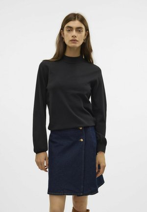 Svart långärmad topp med hög krage, kombinerad med en mörk denim A-linje kjol med guldknappar längs sidan.