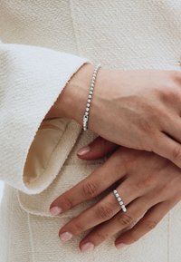 Srebrna narukvica s malim sfernim perlicama i kopčom, uparena s prstenom u istom stilu koji prikazuje red sličnih perlica. Teksturirana pozadina.