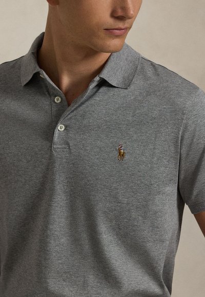 Mees kannab halli polo särki, millel on kaks nööpi kinni ja rinnal väike tikitud logo, kus on joonistus polomängijast hobusel.