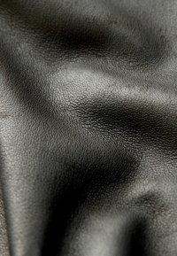 Close-up of wrinkled black leather fabric showing its textured, pebbled surface with light reflecting off the material's folds.