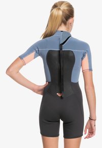 Short wetsuit in blue and black neoprene with short sleeves, back zipper, and pink accents on the sleeves. Smooth texture, athletic fit.