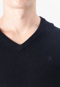 Sötétkék v-nyakú pulóver puha kötött anyagból. Bordás nyakkal és egy kis logóval a mellkason.