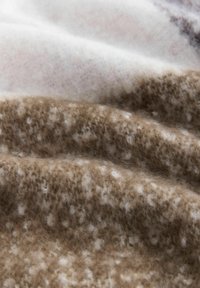 Vlněná látka v odstínech hnědé a krémové, s měkkým, texturovaným povrchem se subtilními bílými skvrnkami a vrstvenými záhyby pro prostorový efekt.