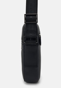 Black crossbody bag made of textured leather, featuring a flat design, adjustable strap, silver hardware, and zippered pocket.