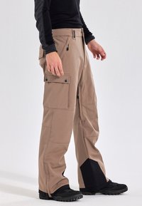 Beige cargobroek met zakken, verstevigde stiksels en zwarte accenten aan de onderkant. Gemaakt van duurzaam materiaal, geschikt voor buitenactiviteiten.
