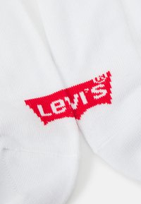 Weiße Socken mit einem roten Levi's-Logo, das nahe der Oberseite eingewebt ist. Das Design enthält ein rechteckiges Logo mit fettem, weißen Text.