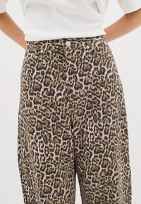Kalhoty s leopardím vzorem vyrobené z měkké látky, s vysokým pasem, zapínáním na knoflík a bočními kapsami. Vzor zahrnuje různé odstíny hnědé a černé.