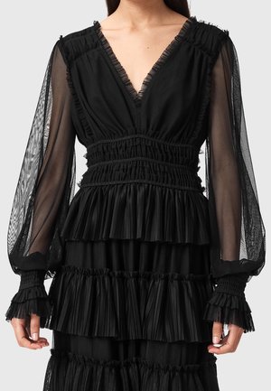 Robe noire avec manches longues transparentes, décolleté en V profond, et plusieurs couches de volants plissés horizontaux sur le corsage et la jupe.