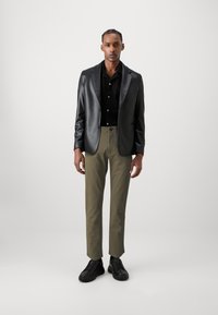 Blazer en faux cuir noir, chemise noire à boutons, pantalon taille olive, et baskets noires, créant un look moderne et épuré.