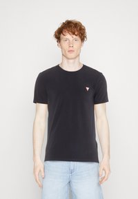 T-shirt nera a girocollo realizzata in cotone, con maniche corte. Presenta un piccolo logo triangolare rosso sul lato sinistro del petto. Design semplice.