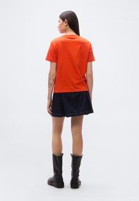 Κόκκινο κοντομάνικο μπλουζάκι με στρογγυλή λαιμόκοψη, σε συνδυασμό με μια σκουρόχρωμη τζιν πλισέ φούστα και μαύρες μπότες μέχρι το γόνατο. Απλό, καθημερινό στυλ.