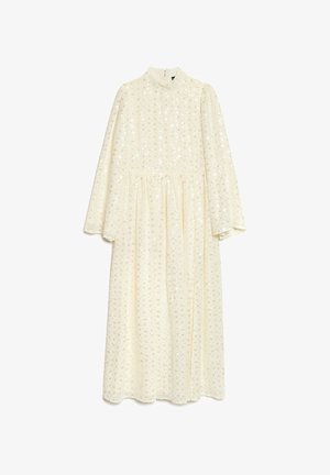 Lang, kremfarget kjole med lange ermer, høy hals og en innsnevret midje. Den har et teksturert mønster av metalliske former over hele kjolen.