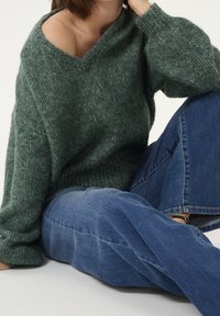 Übergroßer grüner Strickpullover mit weitem Ausschnitt und geripptem Muster, kombiniert mit hellblauen Jeans mit geradem Bein. Weicher und lässiger Look.