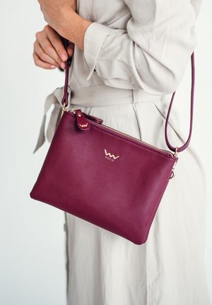Burgundy leather crossbody bag with gold hardware, zip closure, and a small logo accent. Smooth texture and slim rectangular shape.