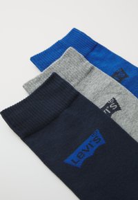 Três pares de meias nas cores azul marinho, cinza e azul brilhante, com punhos canelados e um logotipo em azul escuro em cada par.