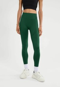 Leggings verdes de tiro alto con paneles texturizados, que cuentan con un acabado suave. Combinados con zapatillas deportivas blancas y calcetines de caña acanalada.